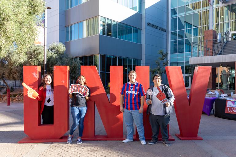 Four students standing in front of large UNLV letters