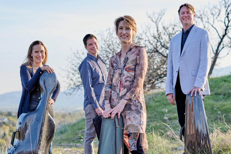 The Fry Street Quartet is outdoors in a green pasture and the four members look towards the camera in this promotional photo.