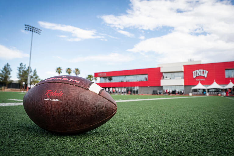 A closeup of a UNLV branded football on the turf at the Fertitta Football Complex