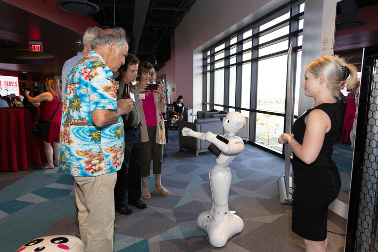 A group of people interact with a Pepper robot, a semi-humanoid robot.