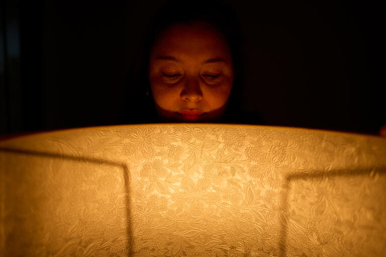 artistic photo of woman in dark room behind large lit lamp shade