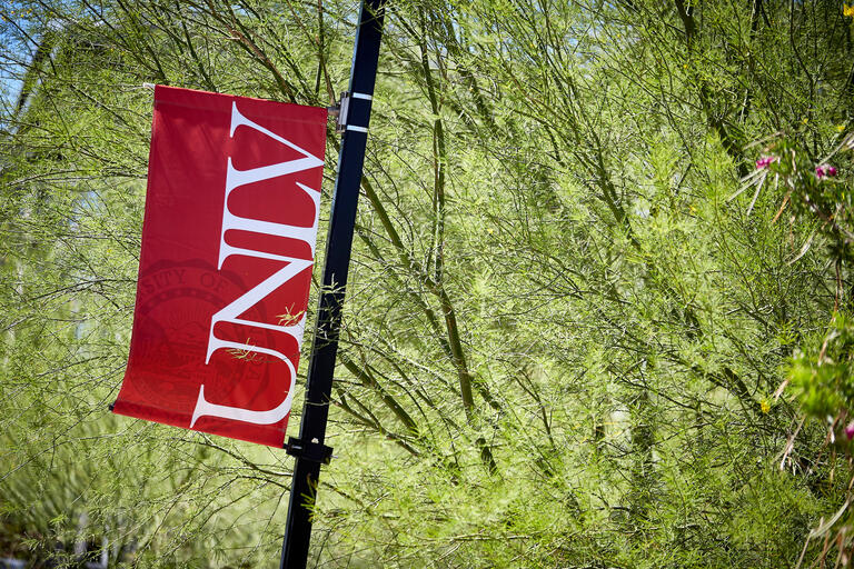 UNLV red flag banner against green leaves of tree