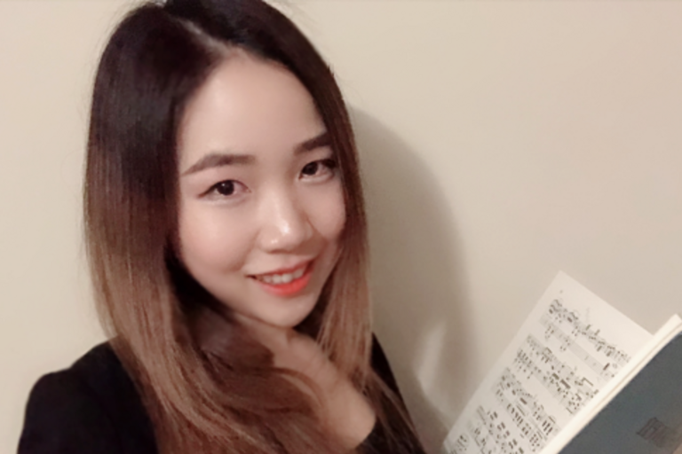 Woman holding a book of music sheets smiling into the camera.