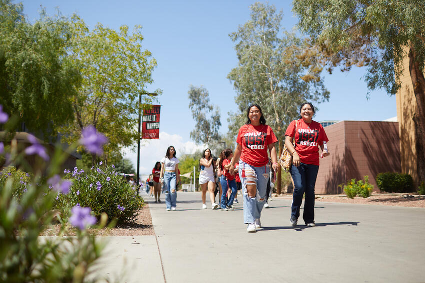 Two students in red UNLV shirts smiling and walking on campus.