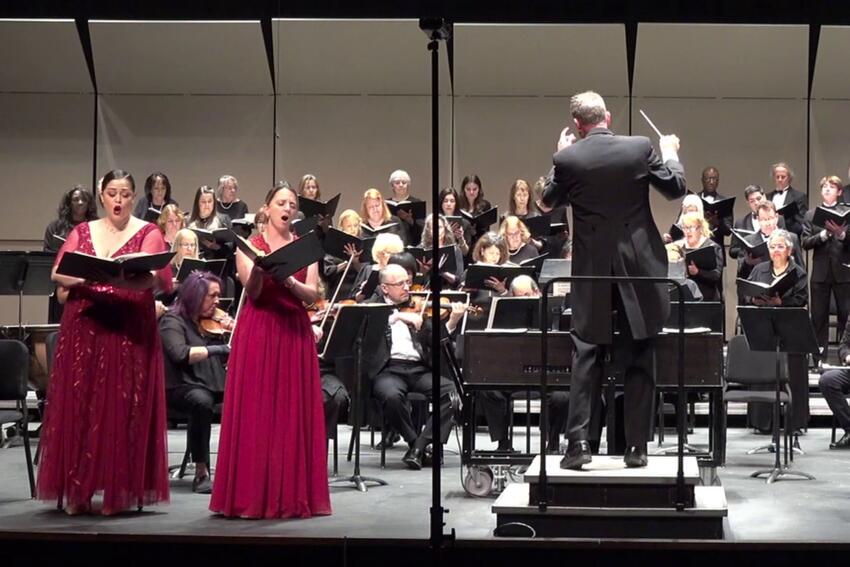 Singers, orchestral artists, and a choir with a conductor on the stage of the Artemus W. Ham Concert Hall.