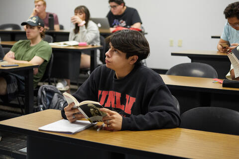 student looking up while holding a book open on a table