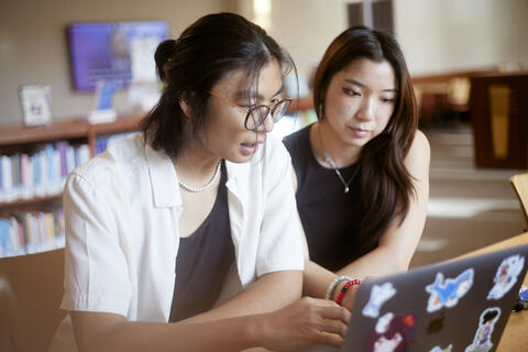 two people looking at a laptop and balloons behind in the background