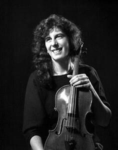 Portrait of Martha Strongin-Katz. She is posed in front of a black backdrop and is holding a violin.