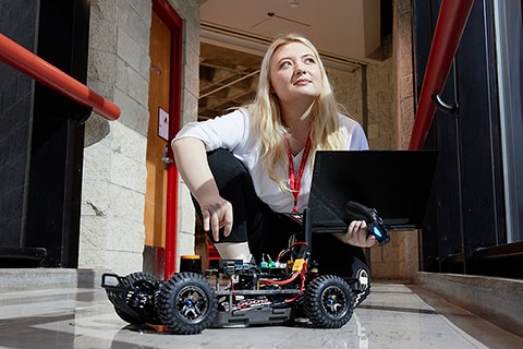 Student with a laptop and small autonomous racing car